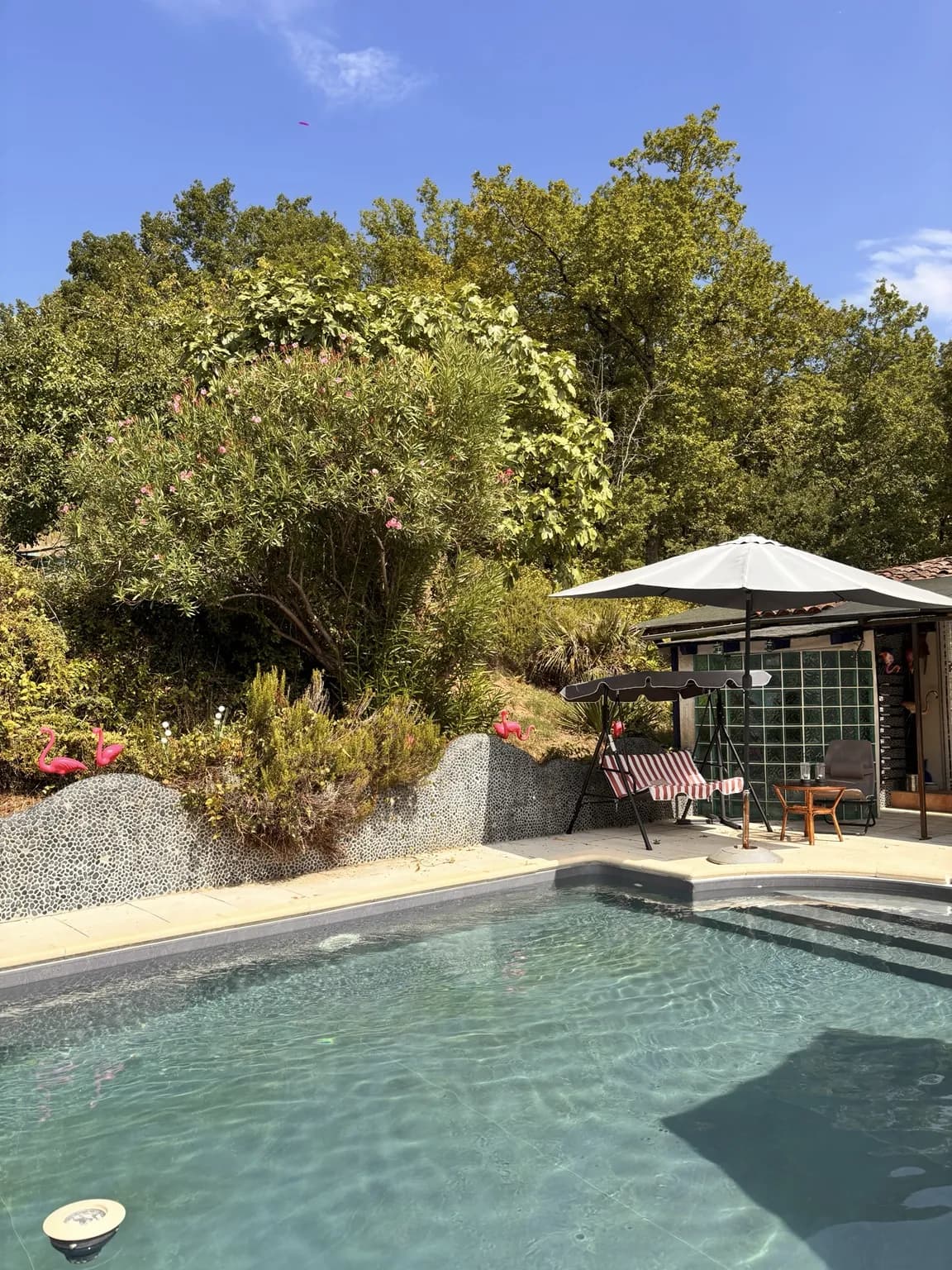 La piscine bordée de son mur en galets, au cœur de la verdure